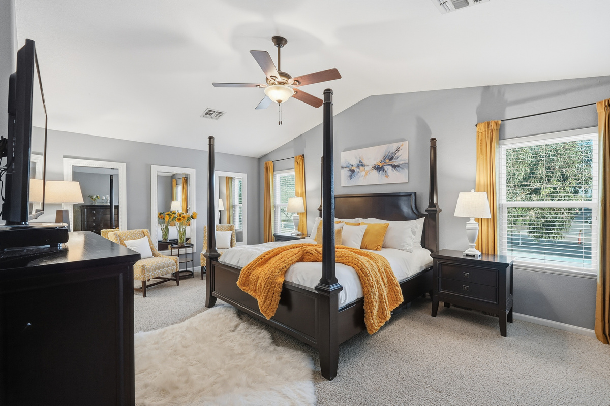Primary bedroom with king bed, four-poster frame, sitting area, ceiling fan, and plenty of natural light.