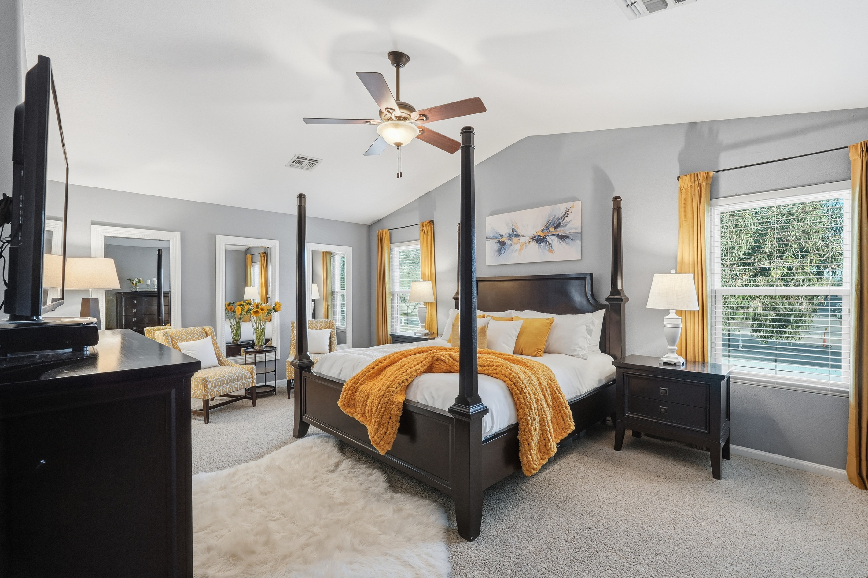 Primary bedroom with king bed, four-poster frame, sitting area, ceiling fan, and plenty of natural light.