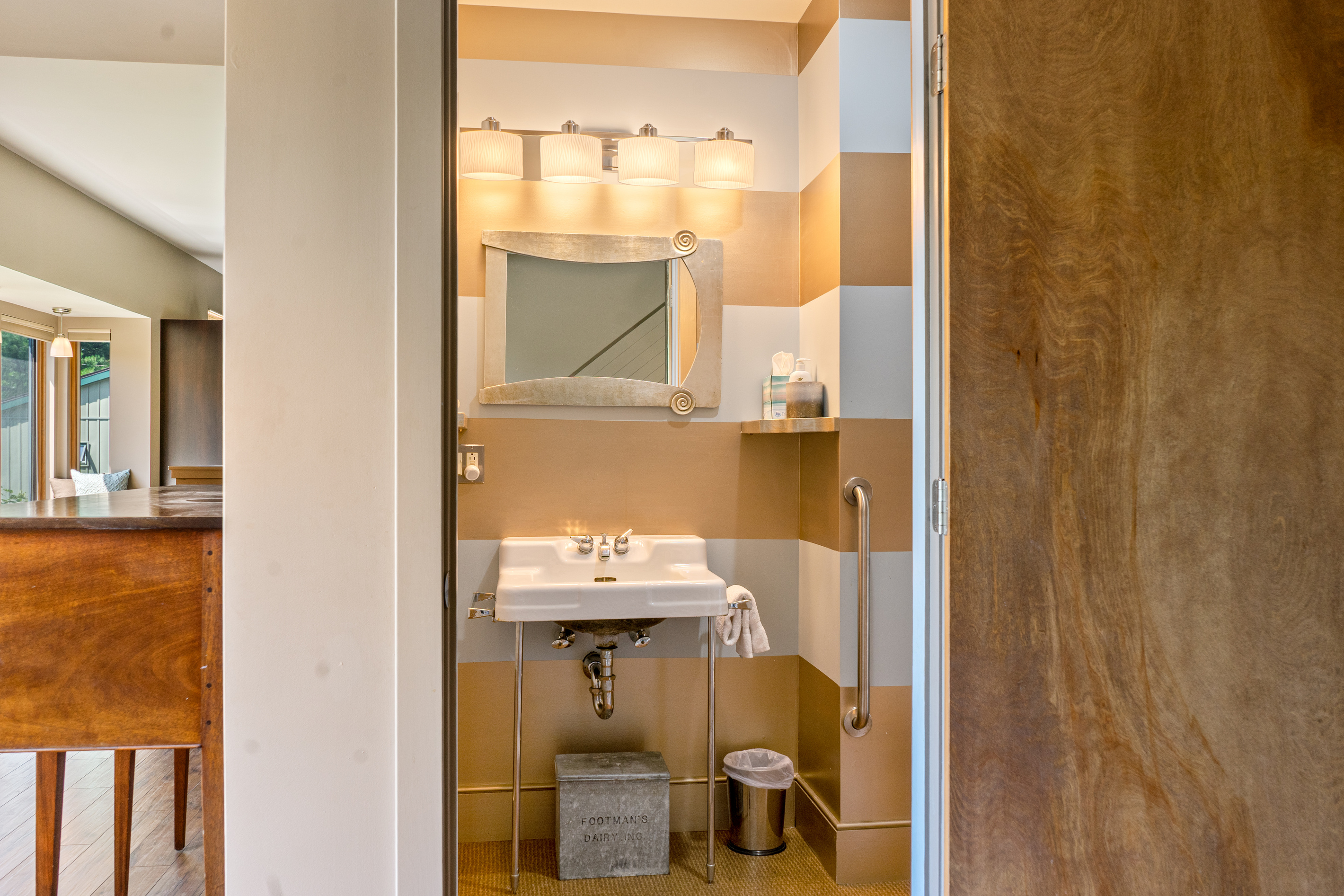 "The Vault" half bath at "The Crag." Features bold metallic striped walls, a vintage chrome console sink, bright vanity lighting, and an accessible grab bar—adding a chic, functional touch to the main living area.