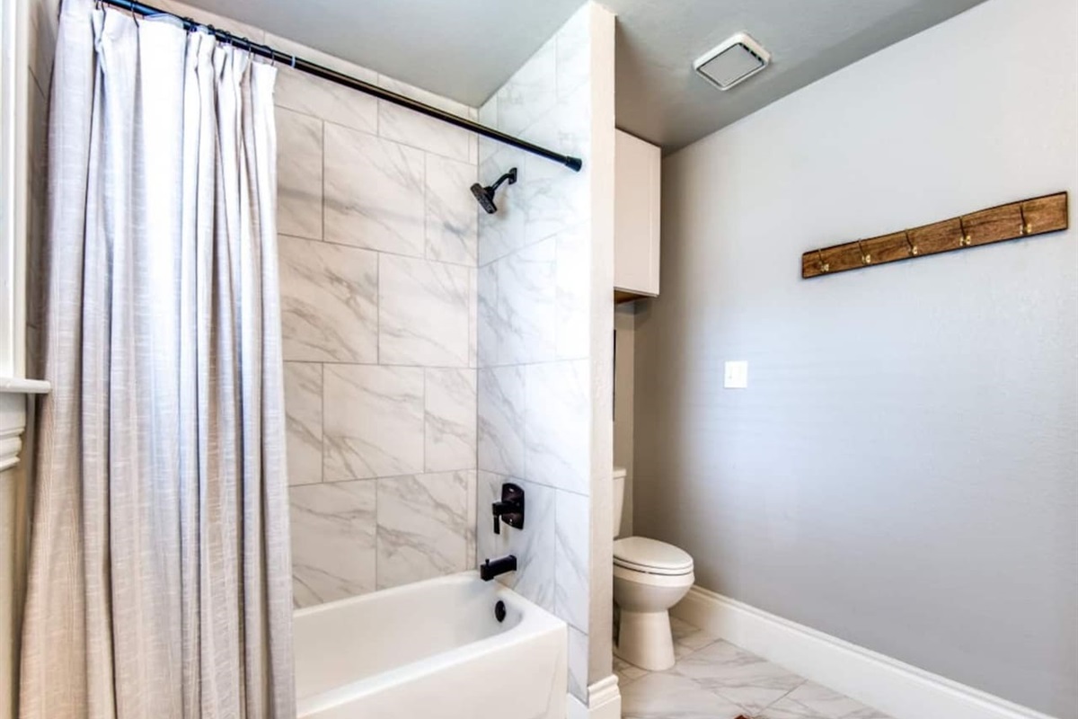Full ensuite bathroom with tub and shower combo, tile surround, and clean white finishes. Stocked with shampoo, conditioner, and body soap. Part of the 2.5 bath layout in this modern farmhouse Airbnb near Lake Ray Roberts in Aubrey TX.