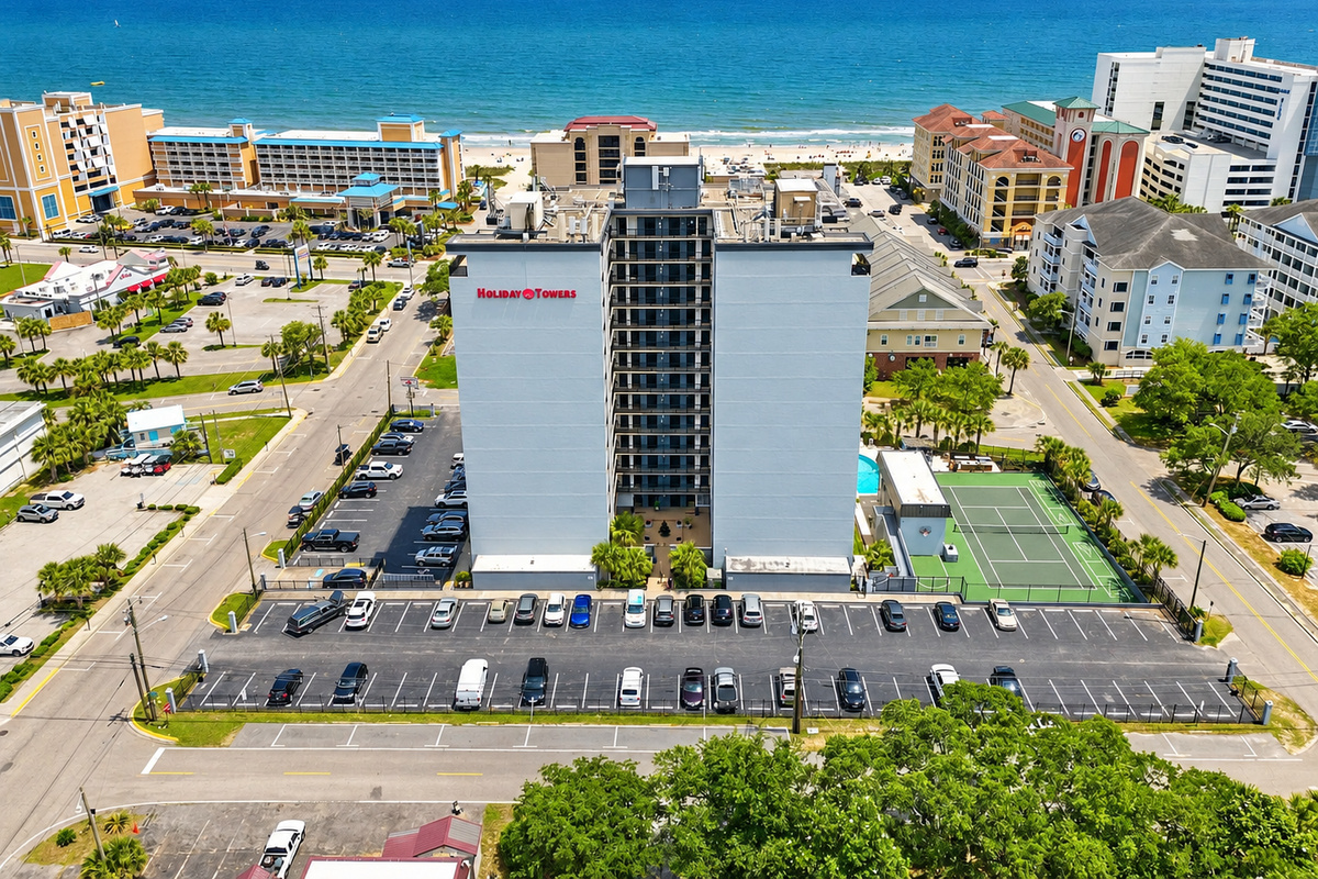 Aerial view of Holiday Towers with shared pool, hot tub, sports court, parking, and Myrtle Beach attractions nearby.