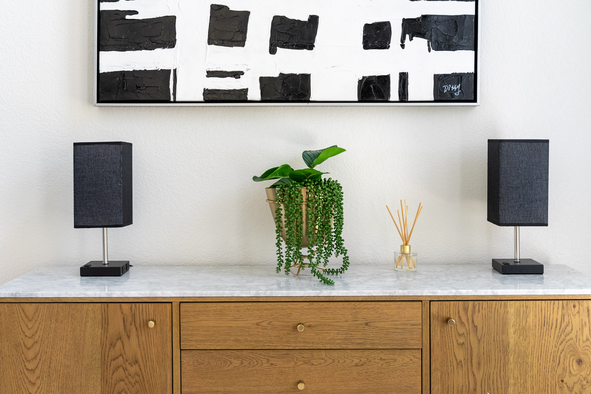 A curated console vignette — modern speakers, trailing greenery, and abstract art.