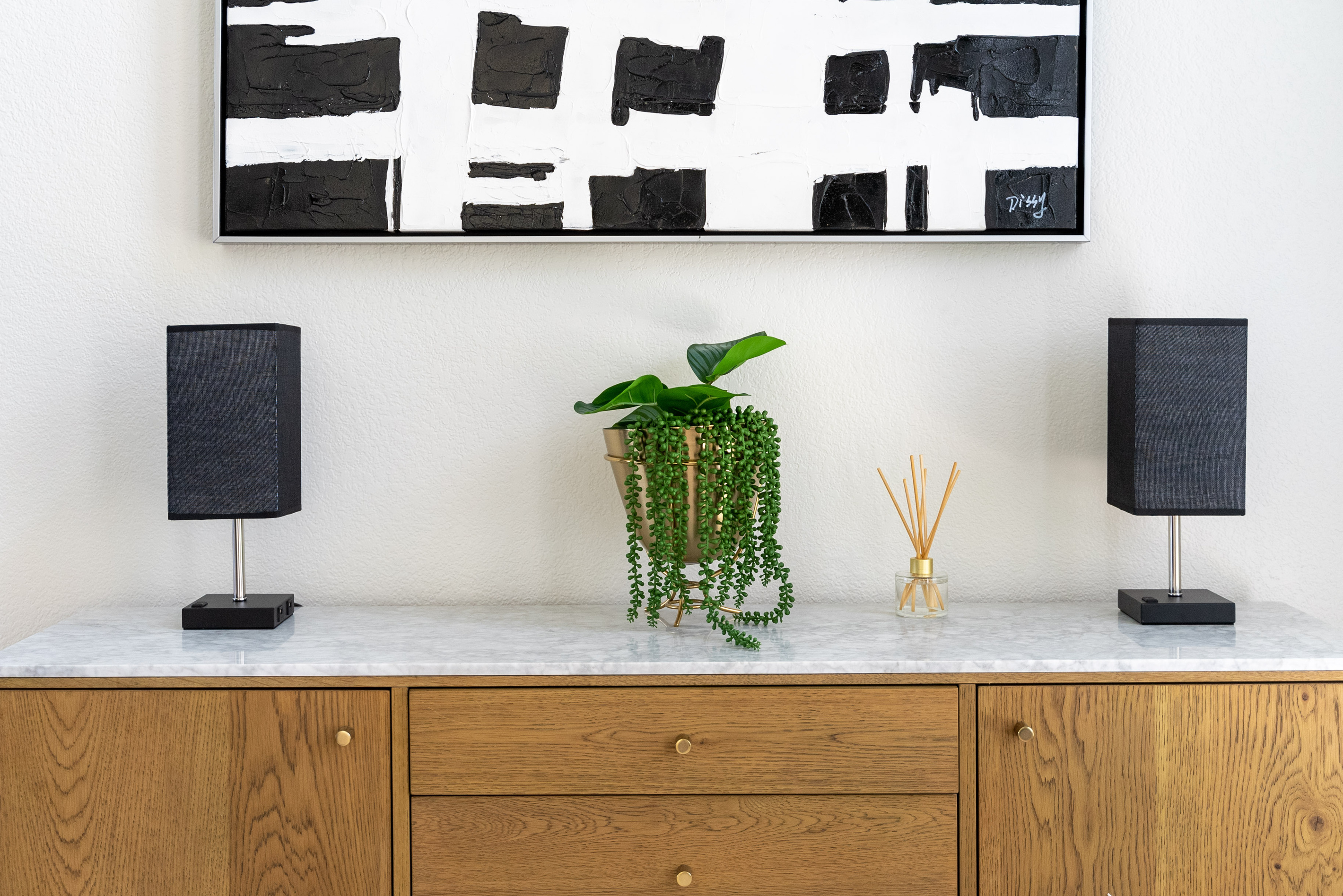 A curated console vignette — modern speakers, trailing greenery, and abstract art.