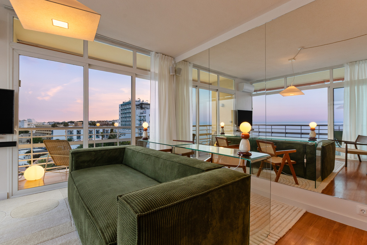 Open-plan living room with balcony access and a calm sunset view over the Mediterranean.