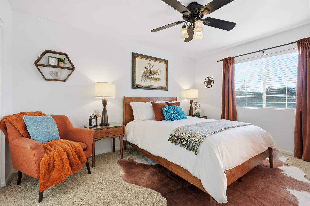 Queen bedroom with accent chair, ceiling fan, bedside lighting, and warm styling for a comfortable stay.
