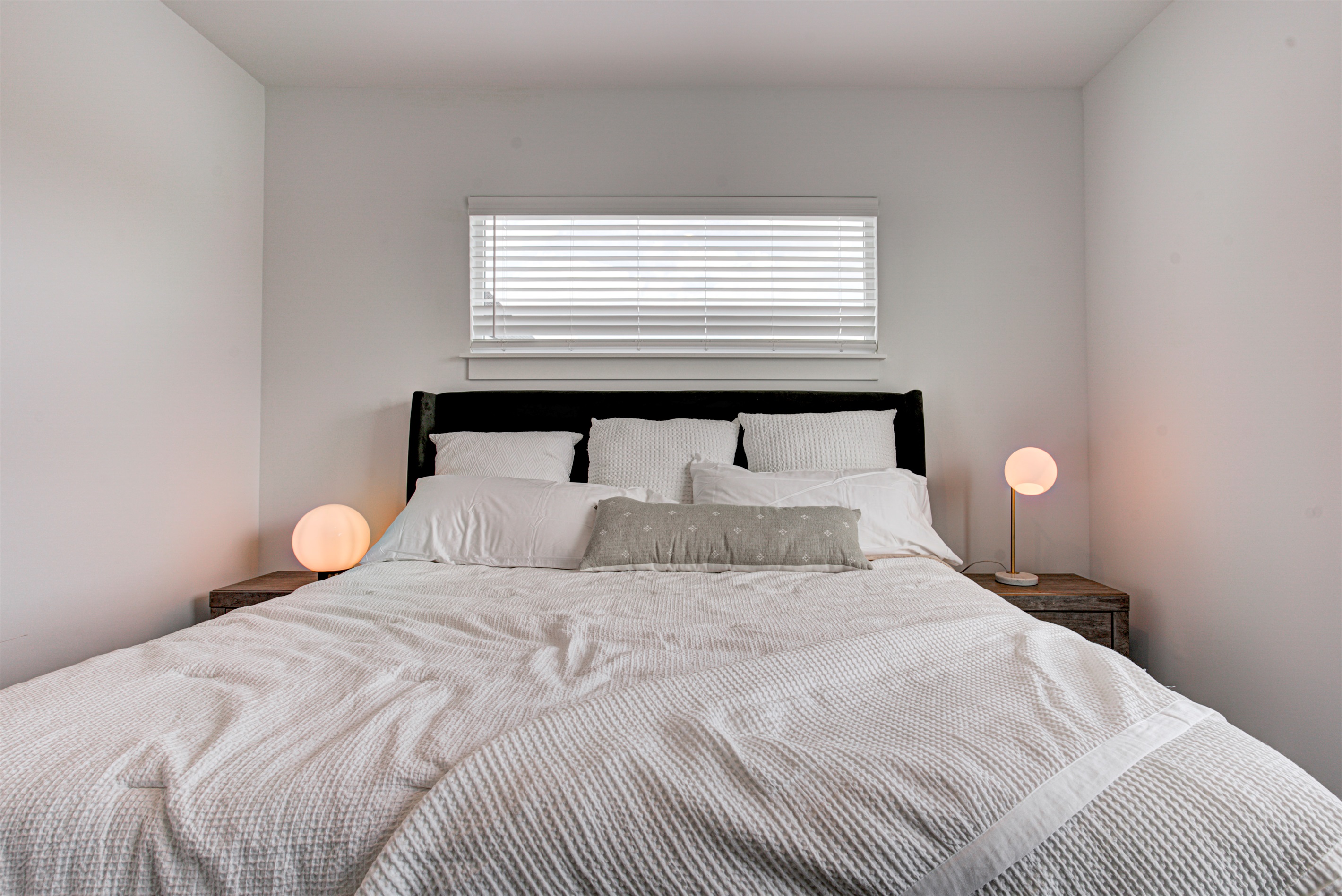 Relax in the serene master bedroom featuring a comfortable king-size bed, soft linens, and cozy pillows. Includes nightstands, lamps, walk-in closet, and full-length mirror for added comfort. 