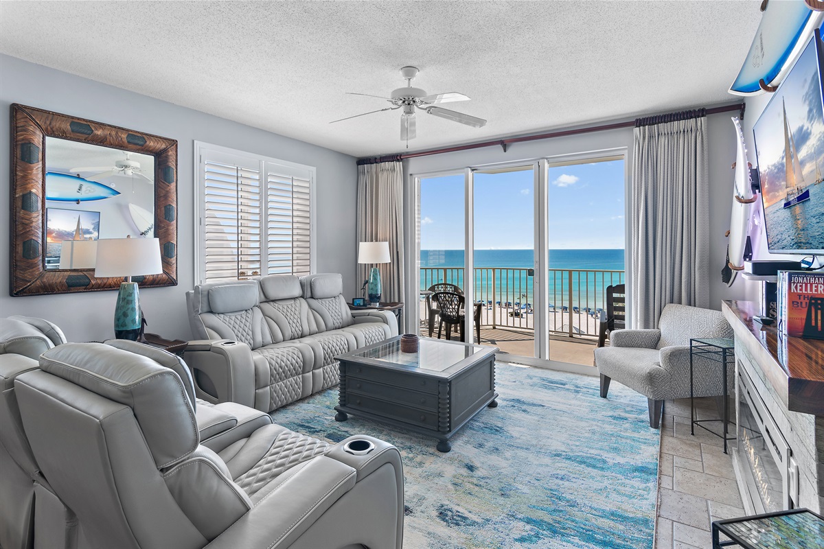 The Gulf View Living Room features a large Smart TV, electric fireplace, backlit surfboard decor, and brand new, leather reclining sofa and loveseat!
