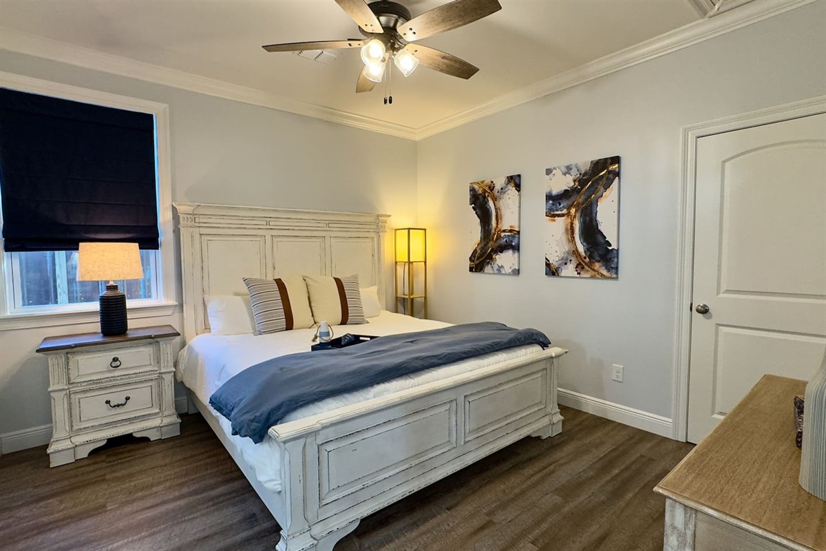 A stylish, light-filled bedroom showcasing a timeless white bed frame, modern artwork, warm wood flooring, and a serene layout designed for restful nights.