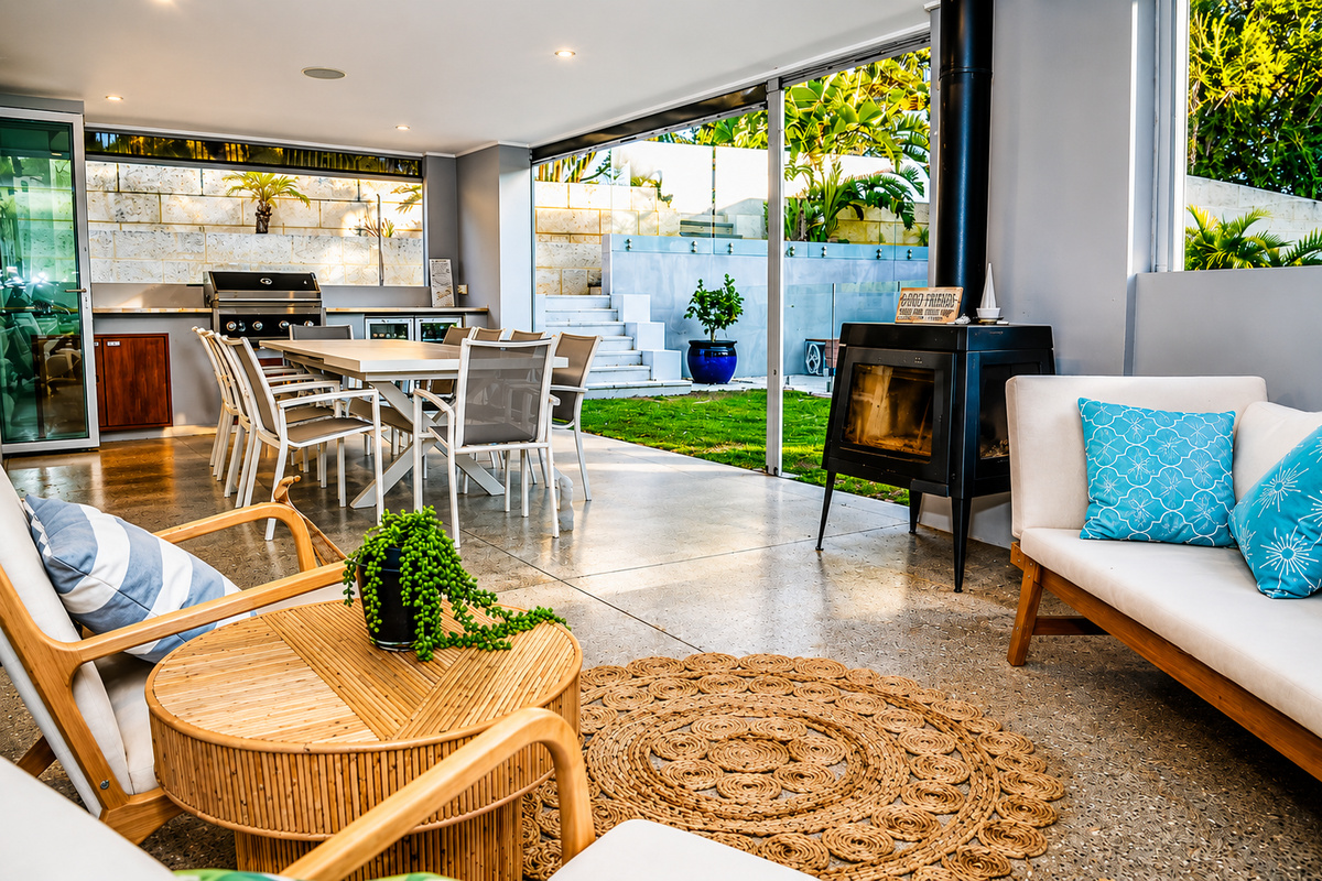 Outdoor entertainment area with lounge seating, dining space, BBQ and an outdoor fireplace beside the private backyard at Sant’s Beach Retreat.