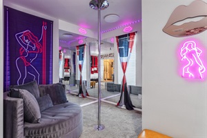 Experience comfort and flair in this serene master bedroom, featuring a luxurious king-sized bed, bold red walls, unique artwork, and a fun stripper pole for a playful touch!