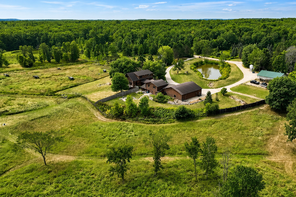 Sweeping aerial view shows the full Northwoods setting, pond, open grounds and surrounding landscape around the House and Lodge.
