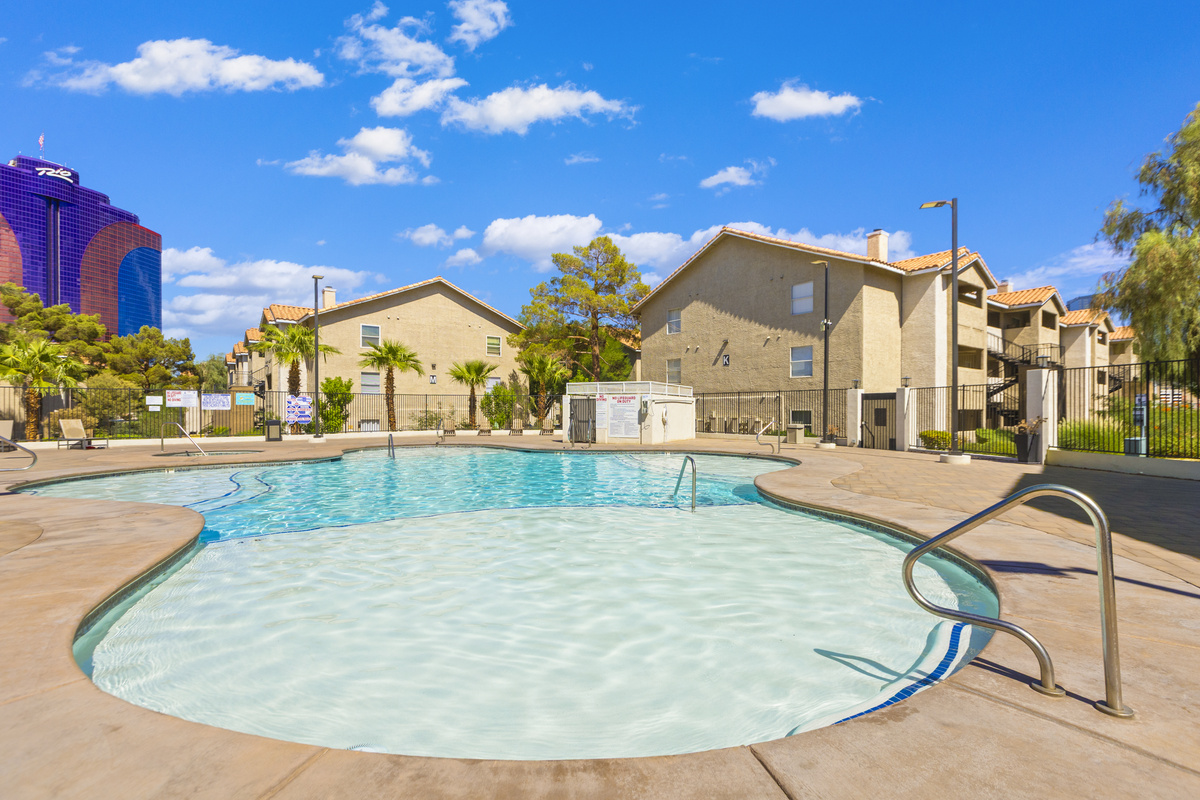 Shared pool area with palm trees, rock features, lounge seating, and a resort-style courtyard feel.
