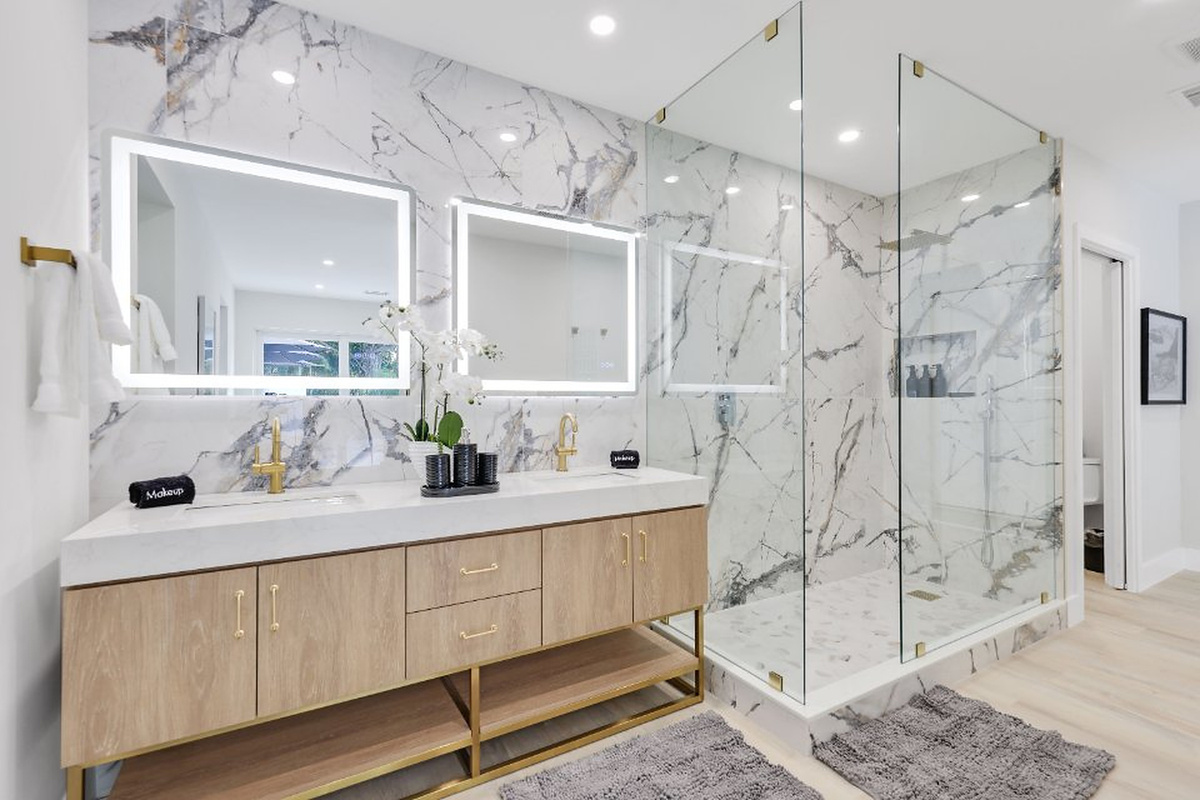 Refresh in a premium bathroom with a double vanity, backlit mirrors, a glass wall shower, marble finishes, and warm gold accents.
