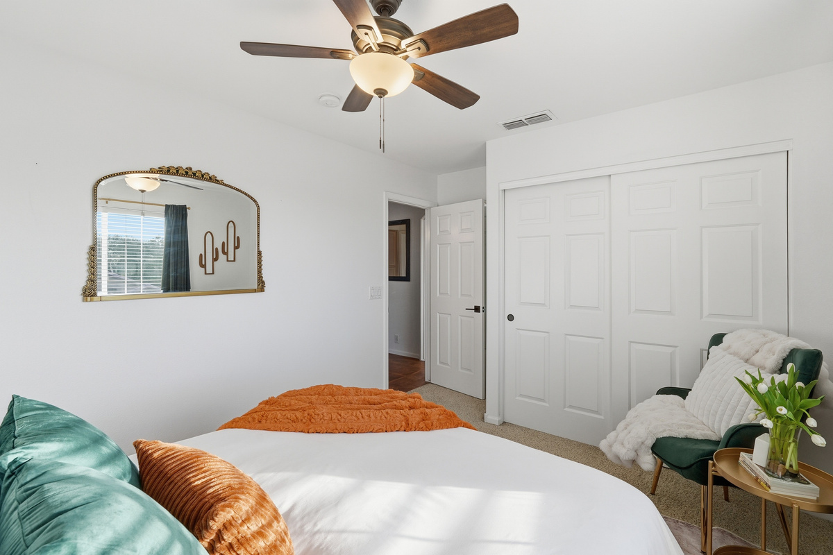 Queen bedroom with ceiling fan, closet storage, accent chair, and warm styling for a comfortable stay.