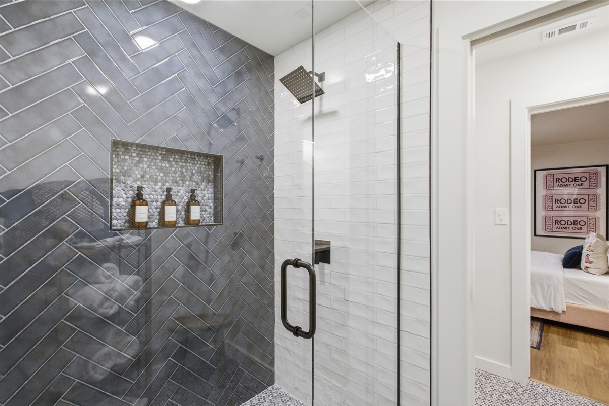 Floor-to-ceiling tiled walk-in shower with designer tile detail. Stocked with Ginger Lily Farms shampoo, conditioner, and body wash. Jack and Jill bathroom near Globe Life Field.