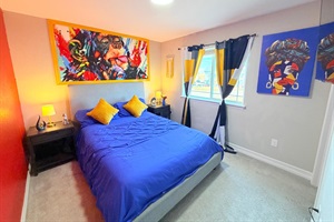 Upstairs cozy queen bedroom with a comfortable bed, bedside tables, playful artwork, & a 55 inch TV. A window lets in natural light, creating a relaxing space to rest and recharge.