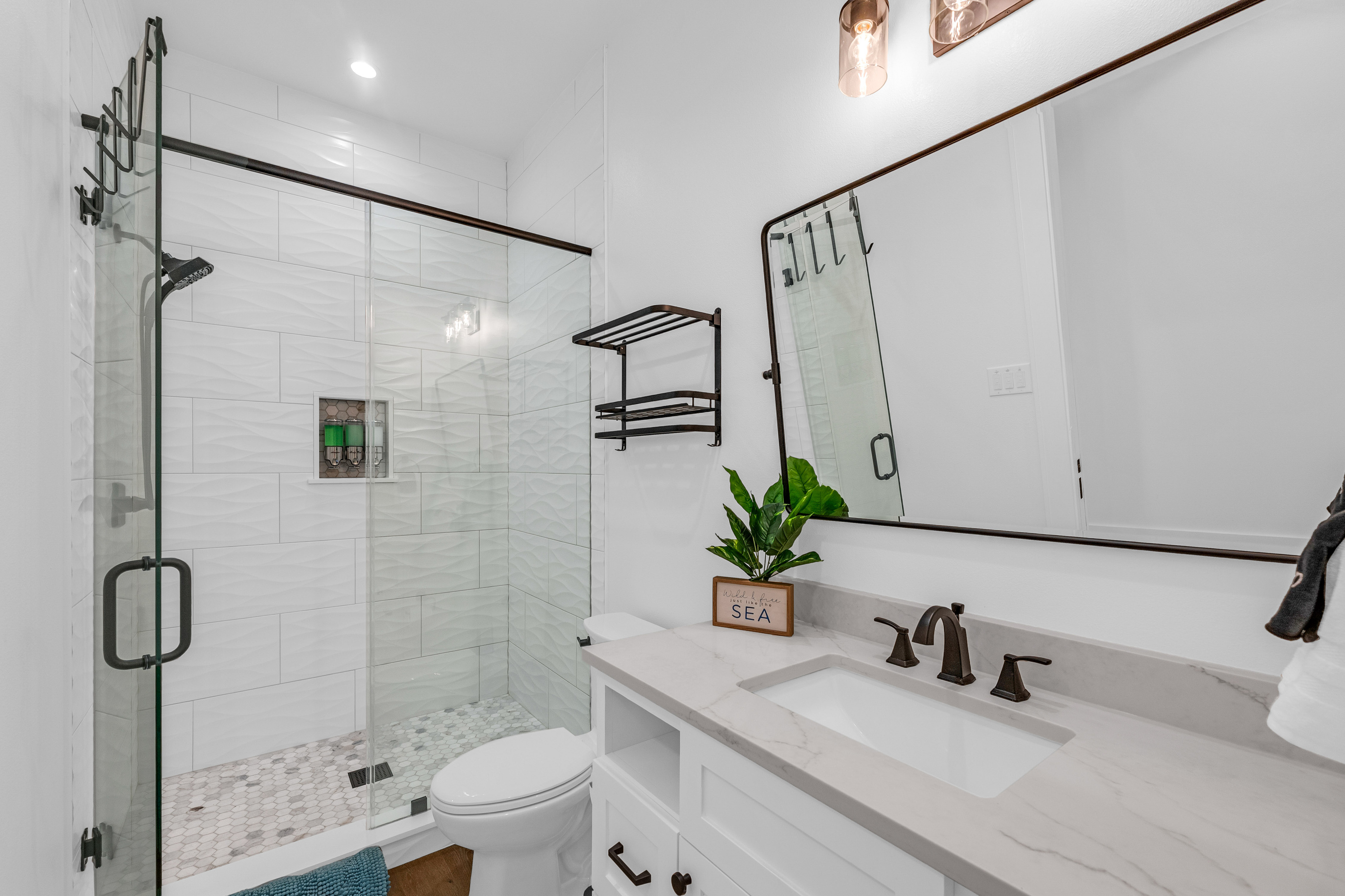 Cair Paravel: A glass-enclosed shower with mosaic tile flooring and a built-in niche keeps this ensuite feeling like a boutique hotel. This ensuite serves the navy king bedroom and features pocket doors from the bedroom to the hallway. 