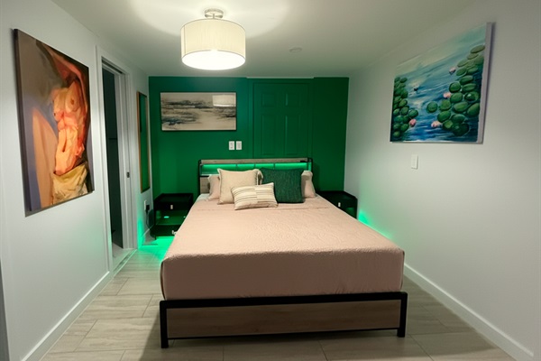Queen bed, warm lighting and green accent wall; double nightstands with convenient bath access.