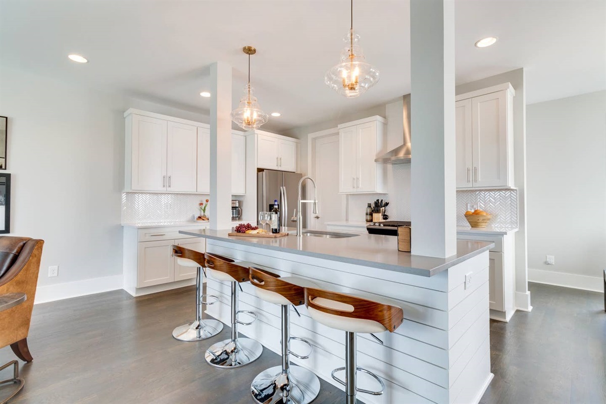 - Sleek white cabinetry & quartz countertops make this kitchen a dream for any chef - Oversized island with stylish wood & chrome stools perfect for casual dining or drinks - Pendant lighting & stainless steel appliances complete the upscale modern look