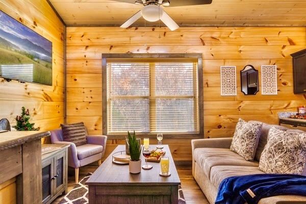 Enjoy the serenity of the Smoky Mountains while relaxing in this cozy living space, overlooking the peaceful wooded area with a charming peekaboo view of the distant mountains through the large window.