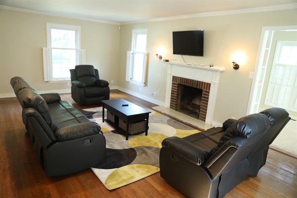 Living Room from Foyer showing Roku TV, wall mounted lamps, fireplace, reclinable single seat, loveseat, and sofa, coffee table