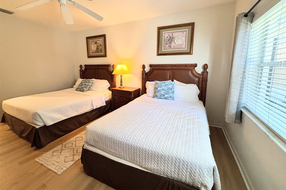 Bright bedroom with two comfortable beds, bedside lighting, and neutral decor.