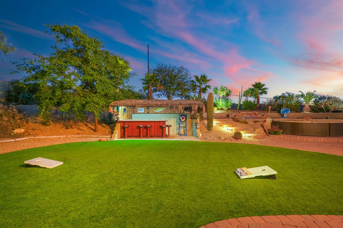 Spacious turf lawn with a tropical tiki bar backdrop, ideal for games, gatherings, and sunset views.