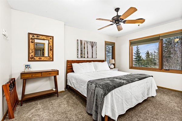 Spacious basement bedroom featuring a comfortable king bed, a ceiling fan for added comfort, and windows that bring in natural light, creating a bright and relaxing retreat.