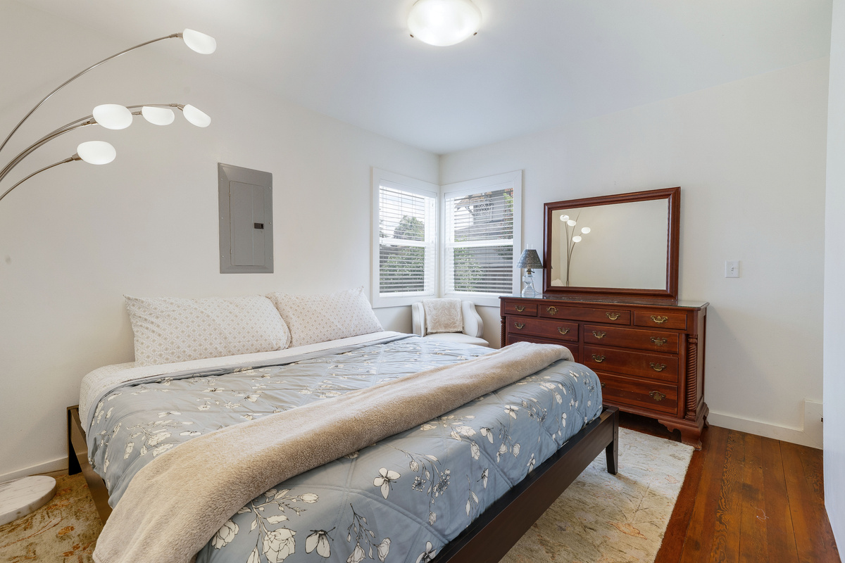 The room closest to the bathroom and the backyard has a king-size bed, a dresser, and a chair by the window. 