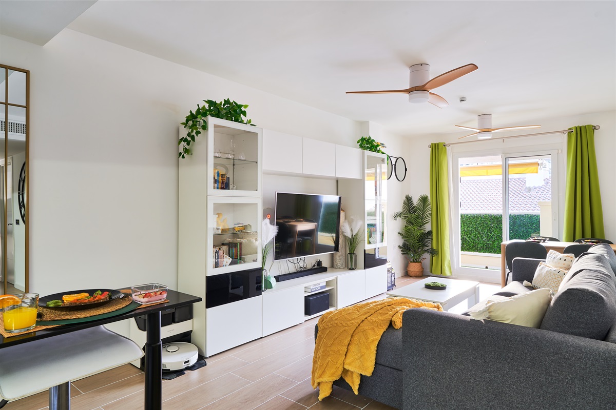Stylish open-plan living room with a modern kitchen, smart TV, and natural light throughout — ideal for relaxing or sharing a glass of wine after a day by the beach.