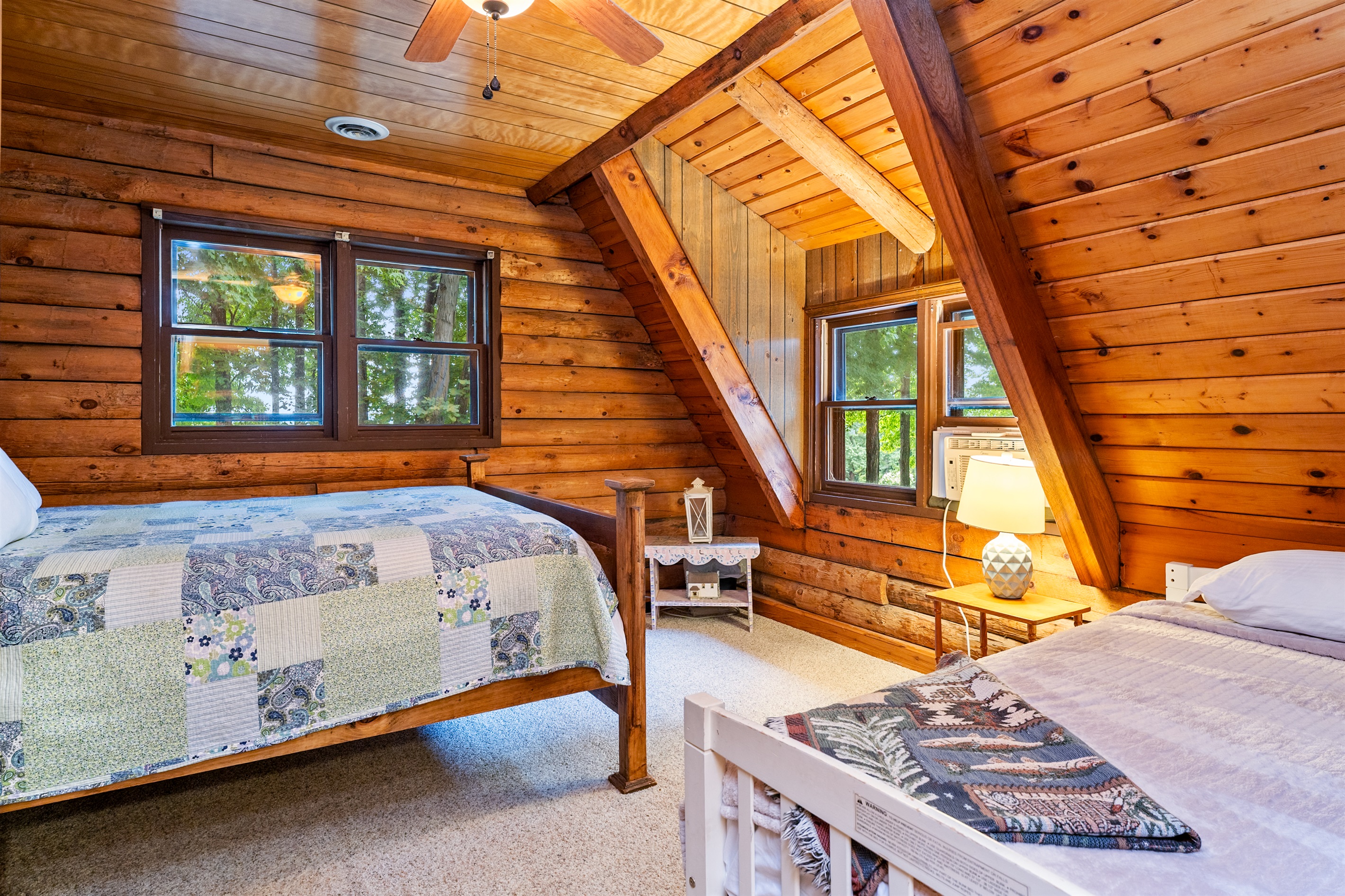 Bedroom #2 Charming log cabin bedroom with a queen bed and twin bed, natural wood beams, and bright windows showcasing forest views.