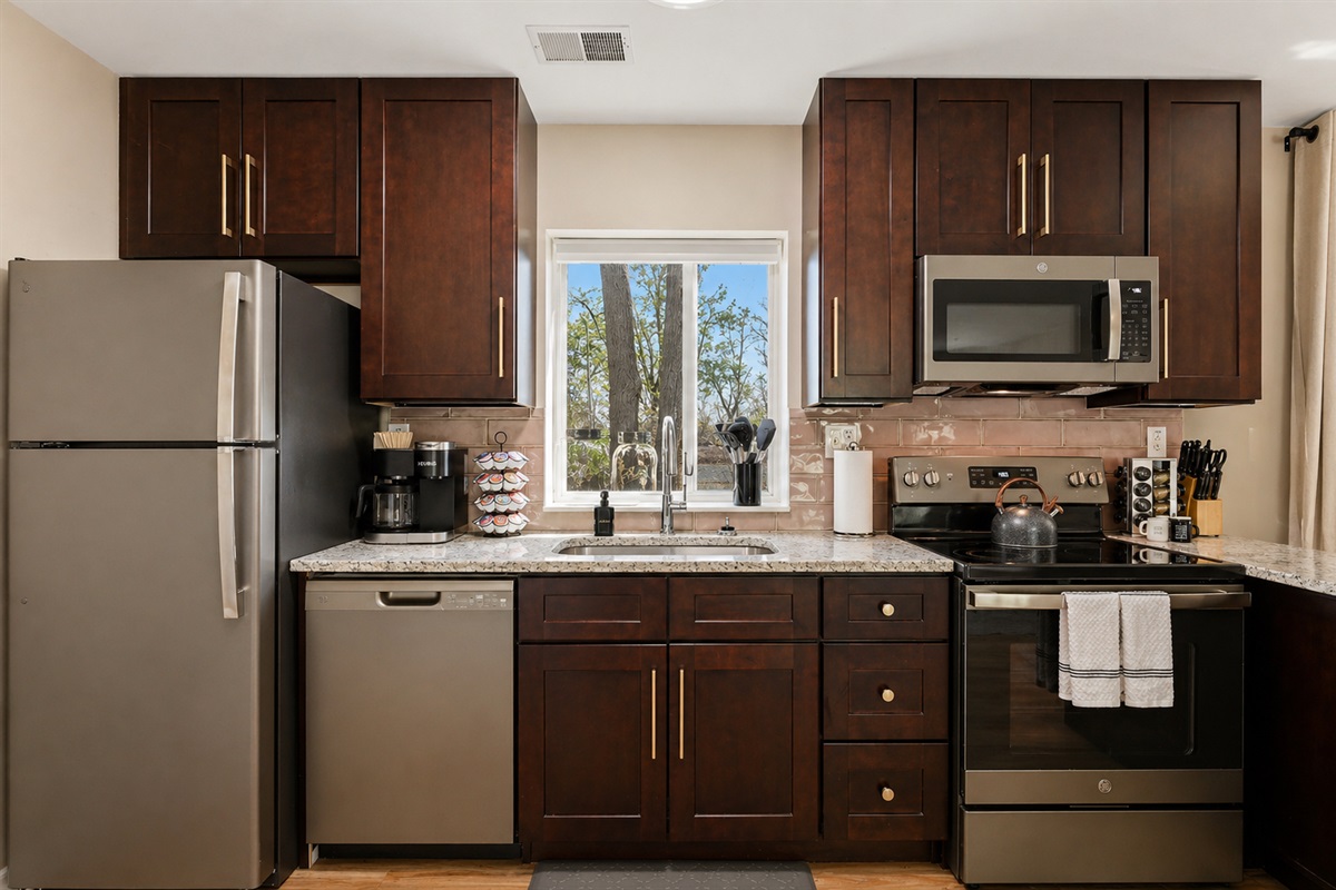 Welcome to a meticulously organized kitchen featuring elegant white cabinets and an array of essential appliances, including a stove, oven, microwave, and a sink. Enjoy the bright ambiance with a window that fills the space with natural light.