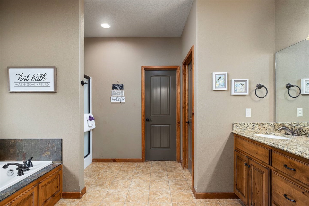 Main level ensuite bathroom with dual vanities, toilet, shower, and jetted tub
