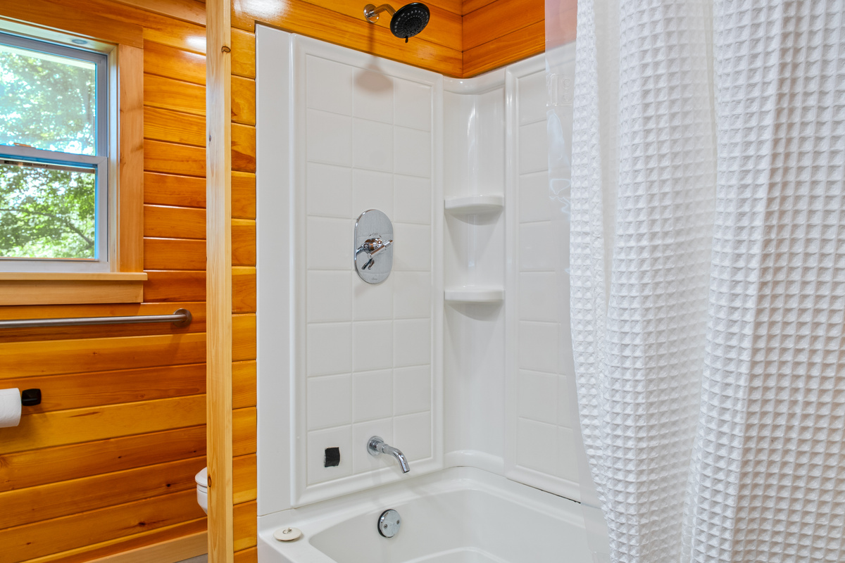 Enjoy a clean, sparkling bathtub and shower combo equipped with built-in corner shelving for your toiletries. This bright station features a modern adjustable showerhead, high-walled white enclosure inserts, and an adjacent window view.