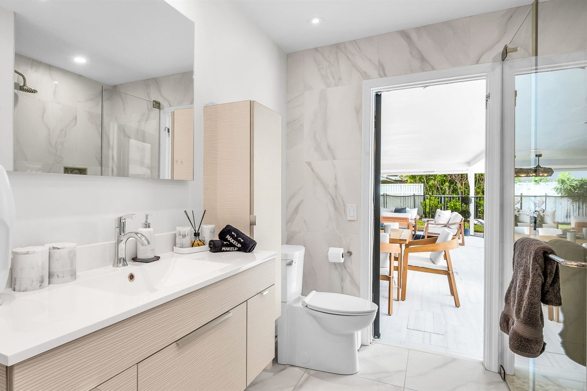 Elegant guest bathroom with sleek modern vanity, designer fixtures, and marble-inspired tile. Features a glass-enclosed shower and direct access to the outdoor lounge and pool area for seamless indoor-outdoor living