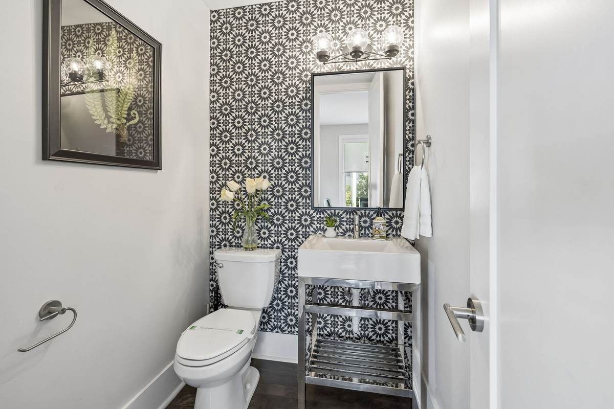 Eye catching black and white floral tile adds personality to this half bath - Sleek chrome vanity with open shelf and bold mirror elevate the modern vibe - Fresh florals, gold accent bin, and minimal d&eacute;cor create a polished guest space