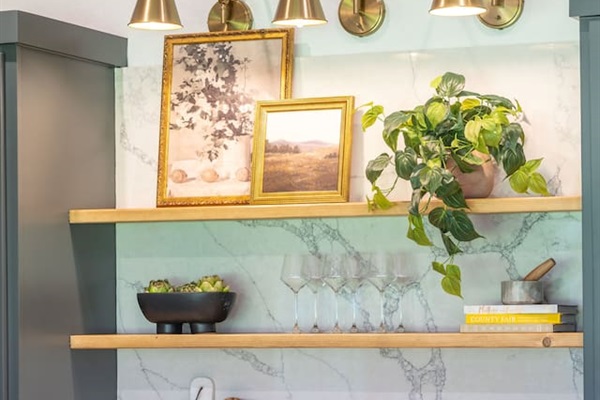 Styled open shelving detail featuring brass sconces, marble backsplash, curated décor, and glassware for a polished kitchen look.