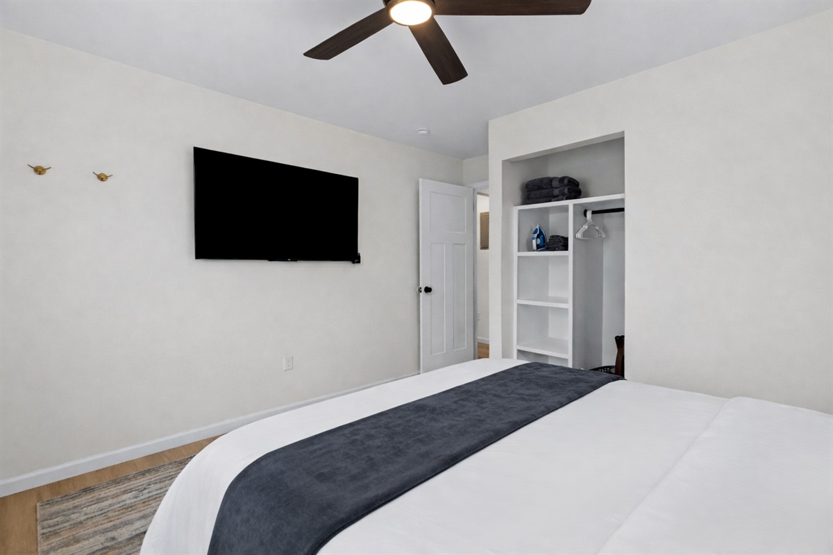 Relax in this well-appointed bedroom with a wall-mounted smart TV, ceiling fan, and open closet storage—designed for comfort and easy living.