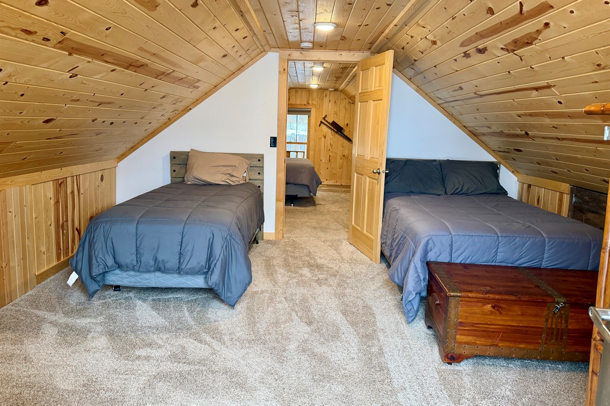 An upstairs bedroom with a cozy layout featuring both a twin bed and a full bed. This walk-through sleeping space is perfect for families or groups, offering flexible accommodations in a warm, cabin style setting.