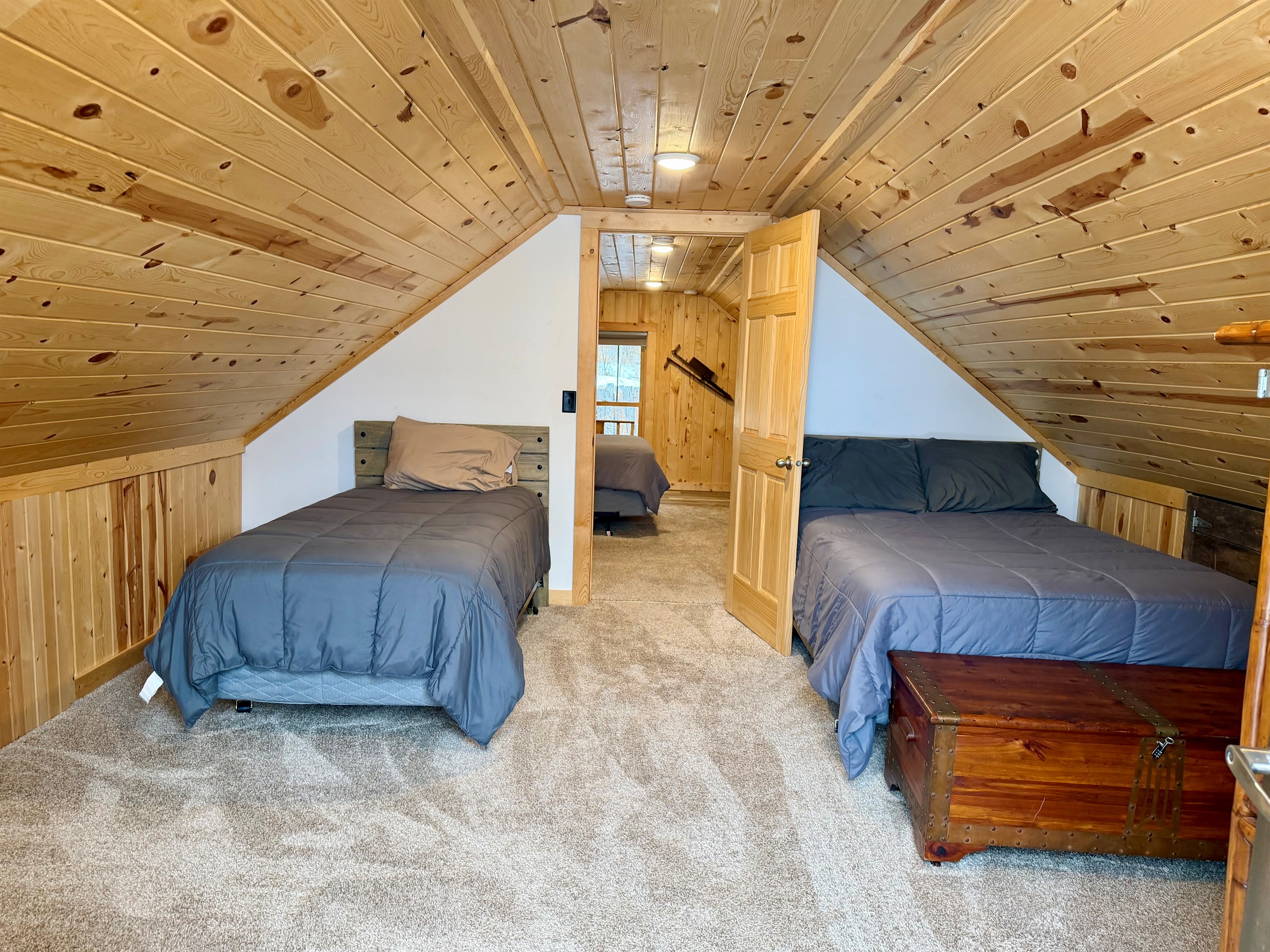 An upstairs bedroom with a cozy layout featuring both a twin bed and a full bed. This walk-through sleeping space is perfect for families or groups, offering flexible accommodations in a warm, cabin style setting.