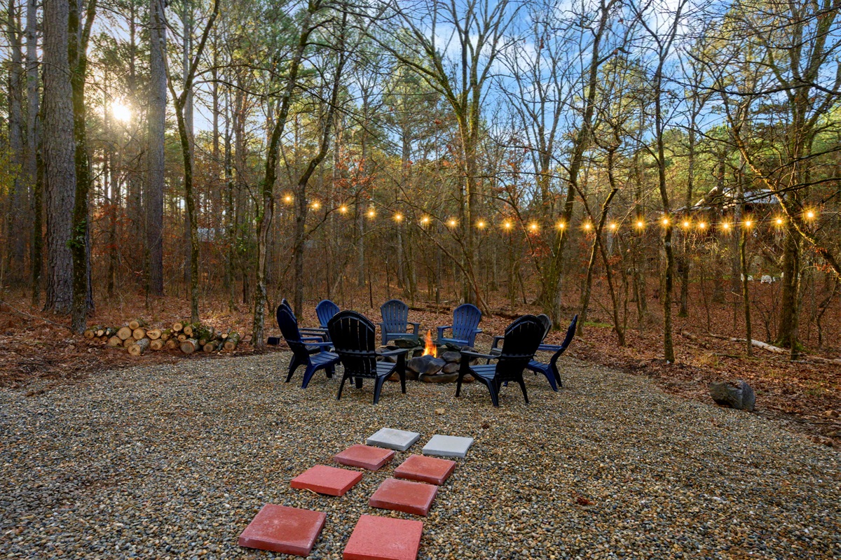 Firepit area lit up by string lights. Firewood provided for guests.