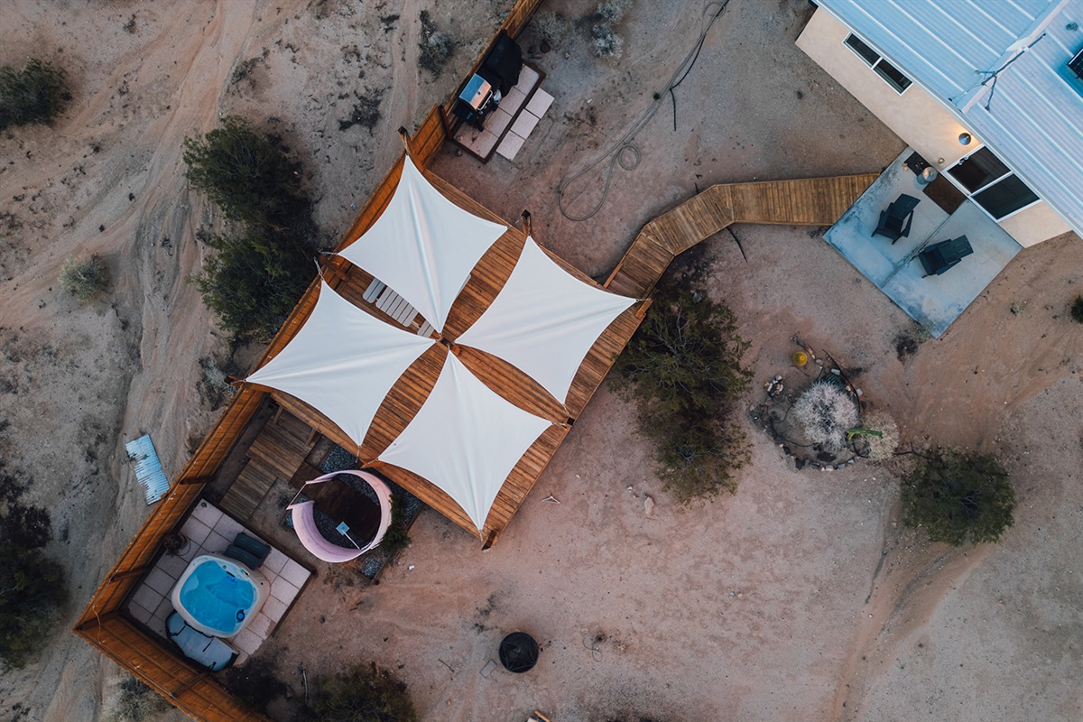 Aerial view of fenced backyard featuring private hot tub, outdoor shower, and lounge deck surrounded by desert landscape.