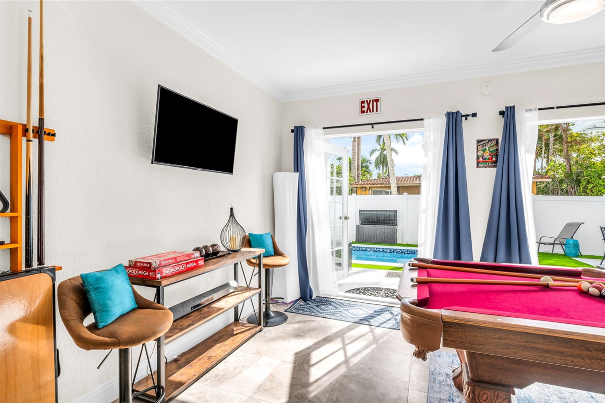 Bright Florida sunroom with a full-size pool table, seating area, beverage cooler, and a streaming TV. French doors open directly to the pool deck for seamless indoor–outdoor entertainment.