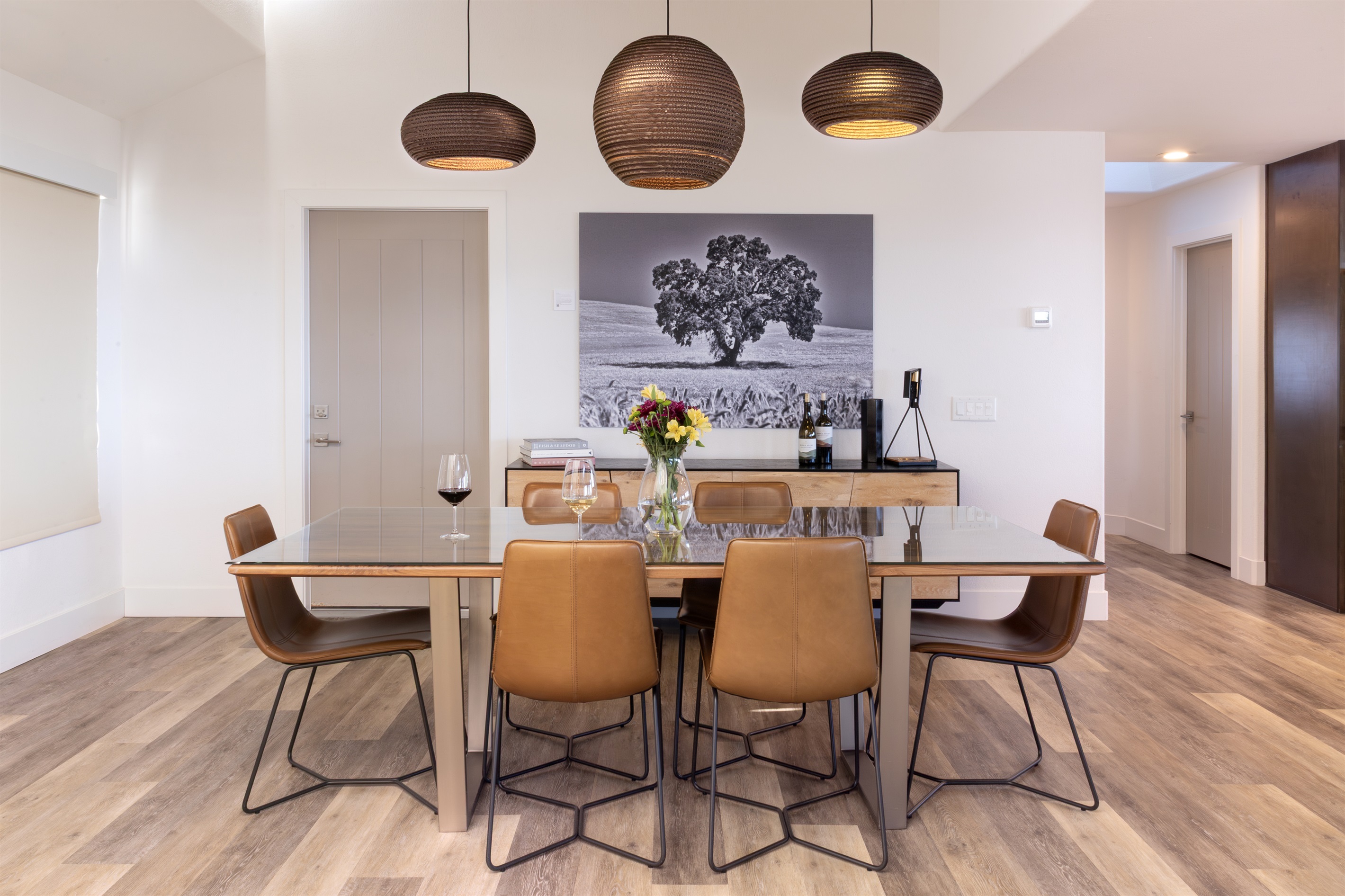 Gather around the table, pour a glass, and stay awhile. The dining room seats eight beneath sculptural pendant lights, with a stunning California oak photograph as the backdrop.