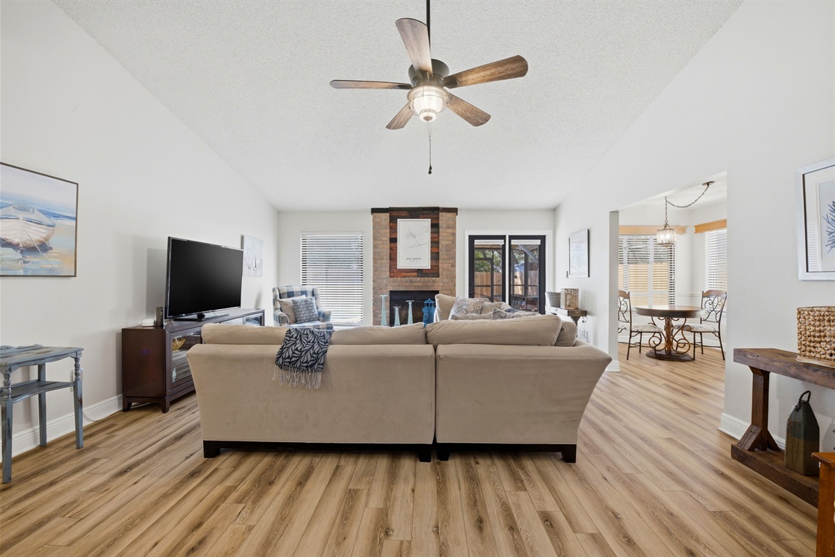 This spacious living area offers plenty of room to relax with family and friends. Cozy sofas, a large TV, and a charming brick fireplace create a welcoming atmosphere, while the high ceilings and natural light make the space feel open and airy.