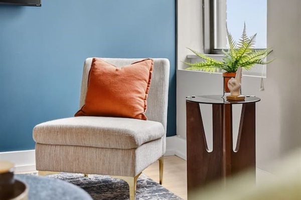 Bright, inviting lounge corner with cozy accent chair, bold blue feature wall, and natural light. Perfect for relaxing, reading, or watching TV in this stylish downtown Des Moines getaway.