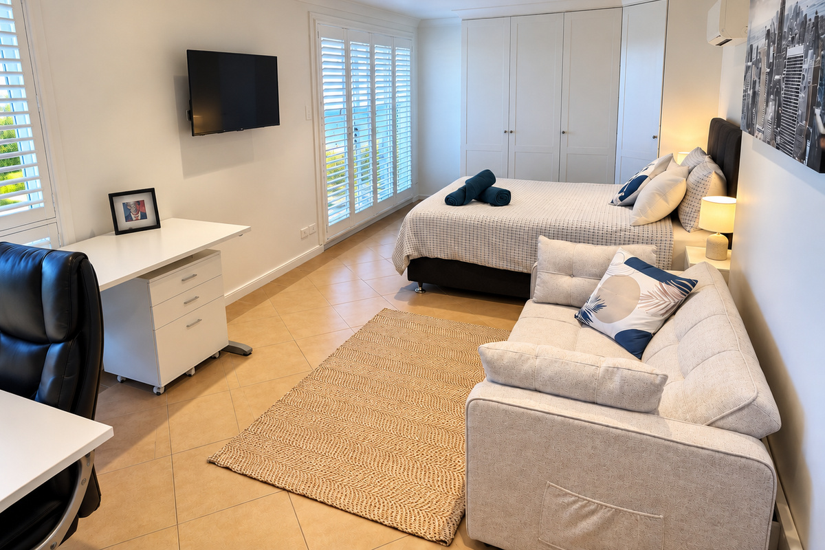 This bedroom at Carinya Coastal Escapes includes built-in robes, tiled floors, timber shutters and an additional seating area.