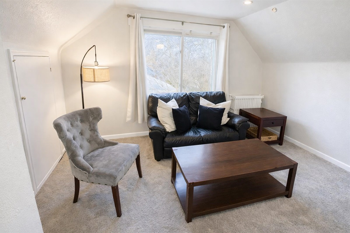 The living room is furnished with a cozy leather couch and accent chair, providing a comfortable seating arrangement. Additionally, there’s a supplementary AC unit to keep you cool during sweltering summer days.