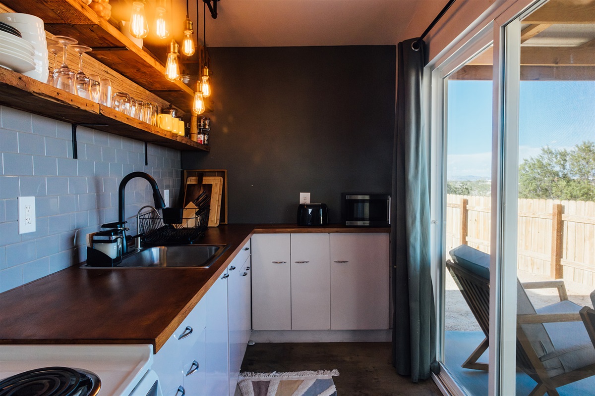 Fully equipped modern kitchen with butcher-block countertops, stylish shelving, and sliding glass doors to the patio.