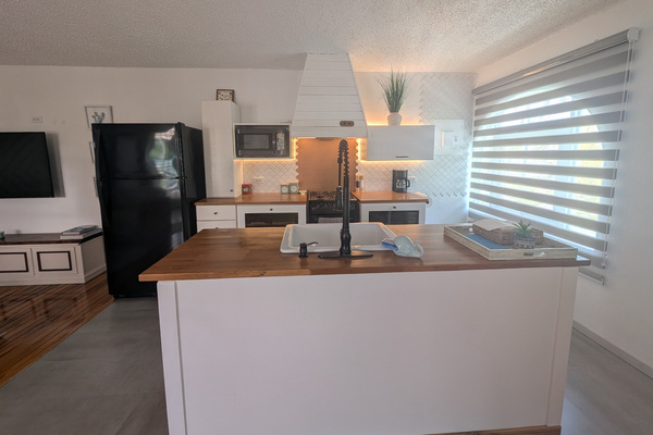 Fully equipped upstairs kitchen at Villa Coral featuring a white central island with a wood countertop, integrated sink, black refrigerator, modern white range hood, and warm ambient LED lighting in Dorado, Puerto Rico.
